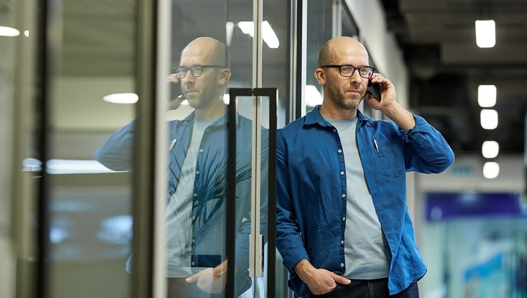 ein Mann, der neben einer Glaswand mit einem Handy telefoniert