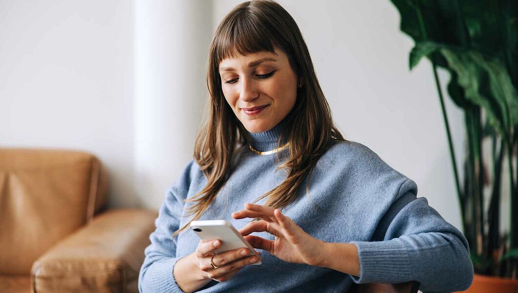 eine Frau, die auf einem Stuhl sitzt und auf ihr Mobiltelefon schaut